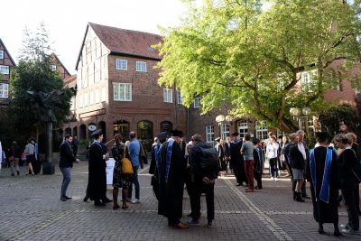 Absolvent*innen und Gäste warten vor dem Glockenhaus