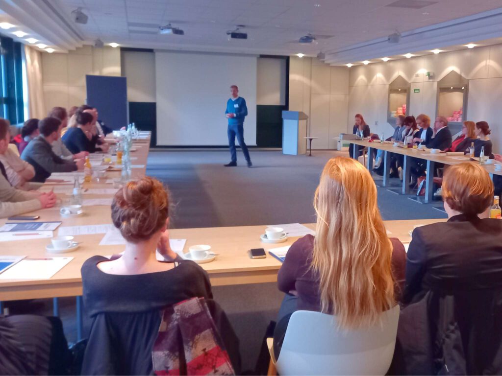 Die Studierenden und das CSM-Team sitzen an einem langen Tisch in U-Form. An der Frontseite des Raumes steht eine vortragende Person.